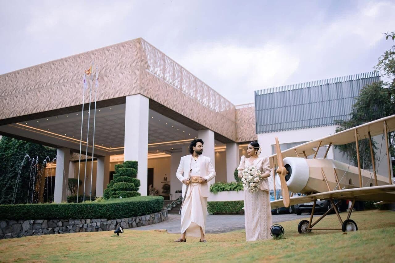 A bride and groom on the lawn in front of the hotel entrance, beside a vintage aeroplane