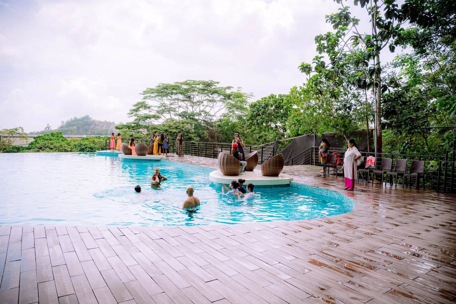 Guests in the infinity pool, with round wicker loungers and green hills beyond
