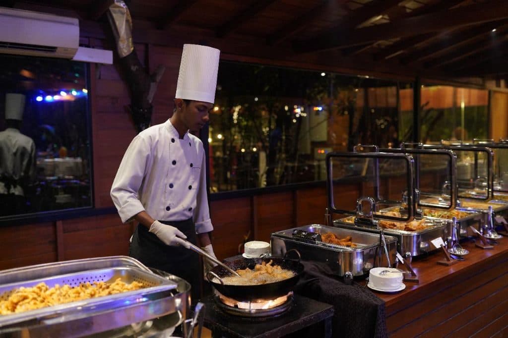 A chef cooking at a live station beside chafing dishes