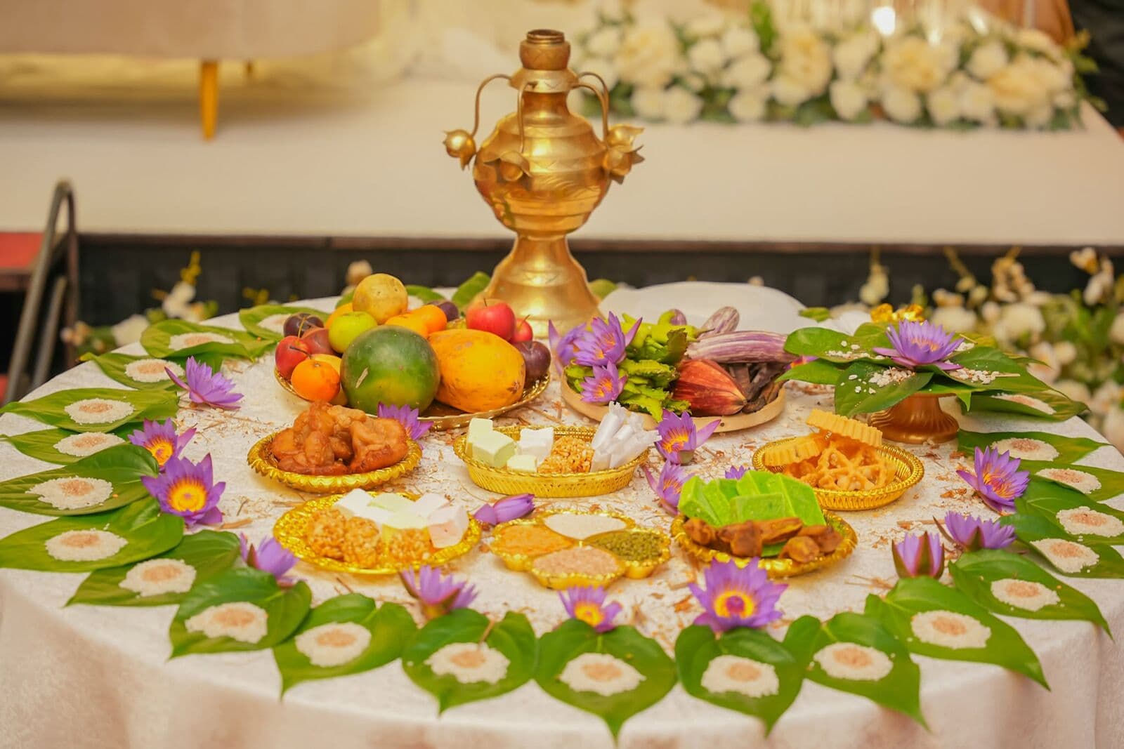 A traditional table of fruit and sweets on banana leaves with a brass pot