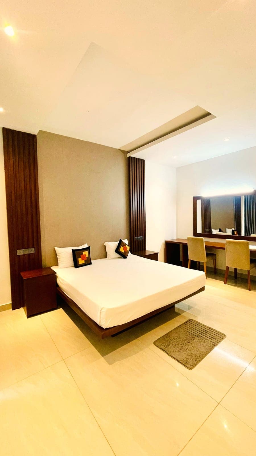 A bedroom with a wide bed, vanity and dark curtains