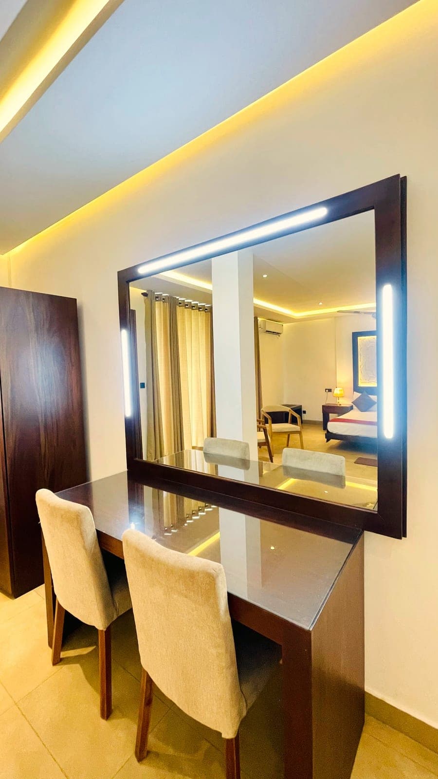 A dressing table with a lit mirror and two cream chairs