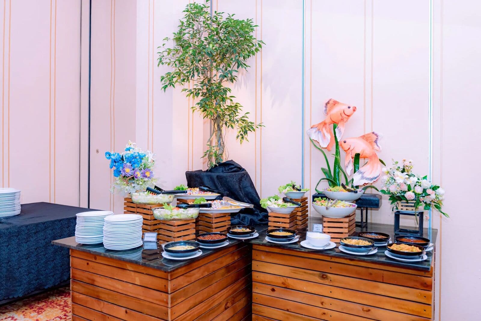 A buffet counter of salads with flower arrangements and a small tree