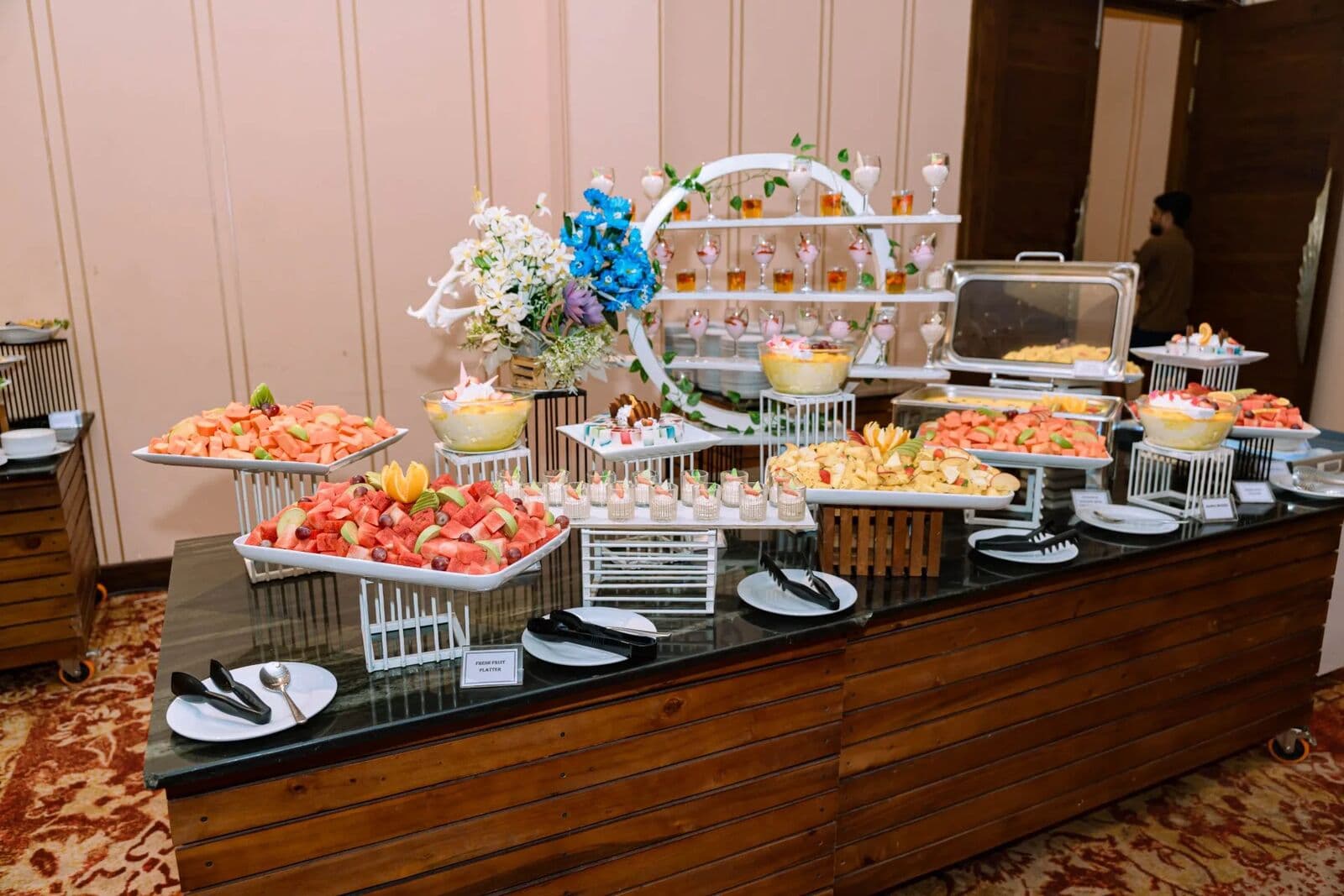 A dessert table of fruit, puddings and cakes beside a flower arch