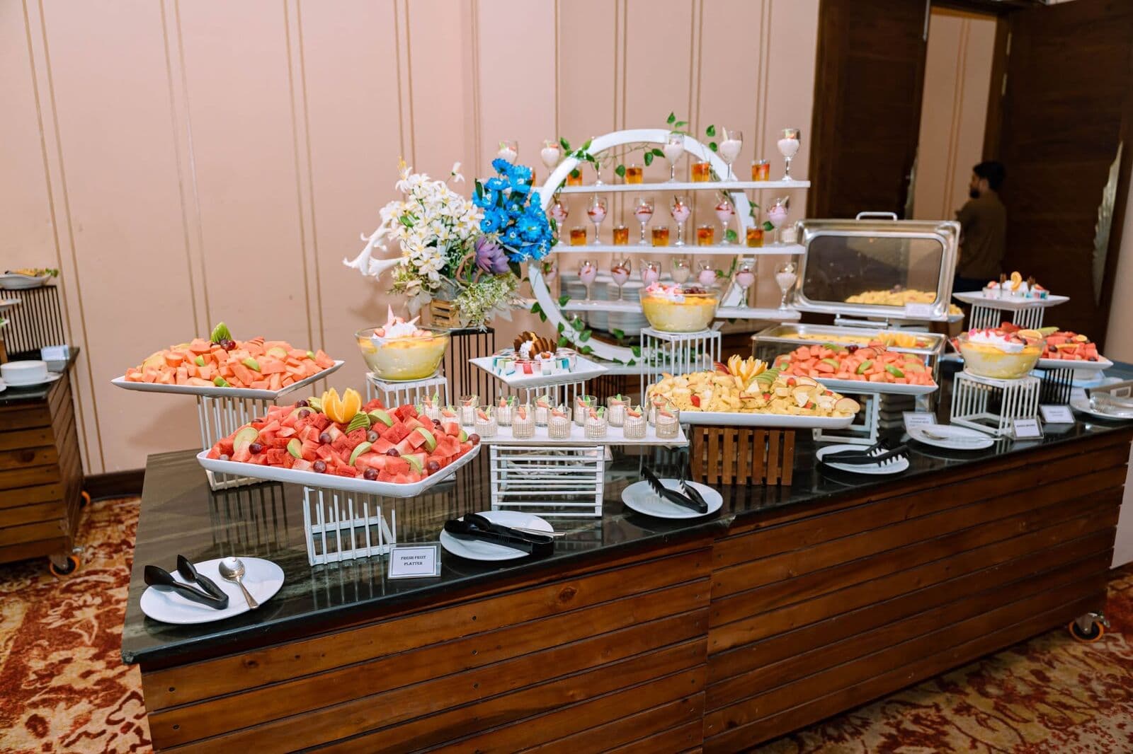 A buffet counter of fresh fruit, desserts and a tiered display with flowers
