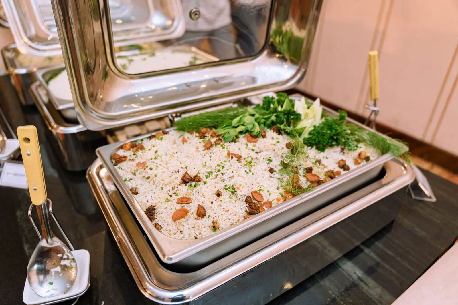 A chafing dish of rice topped with cashews and fresh herbs