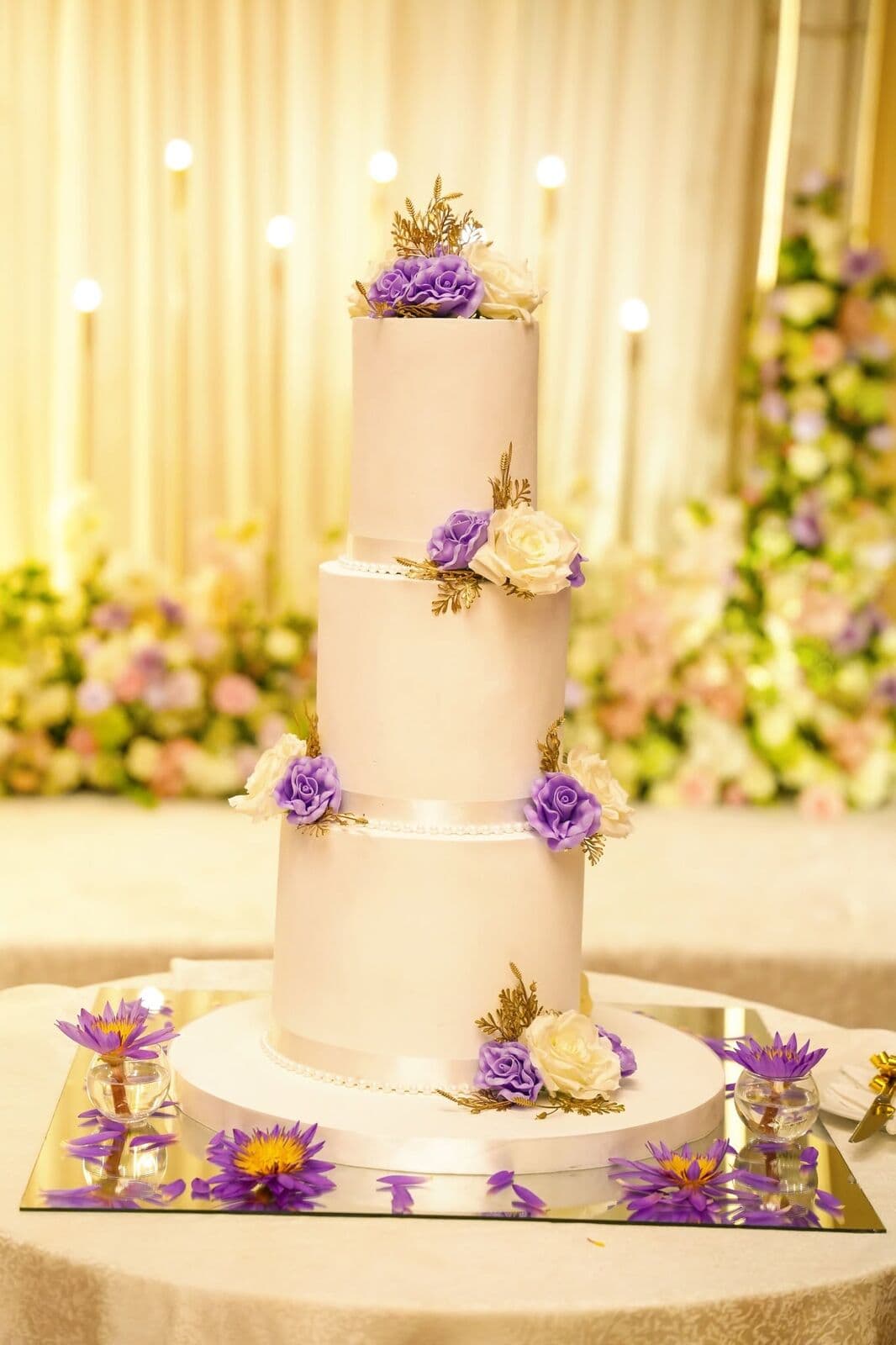 A white three-tier wedding cake decorated with purple flowers