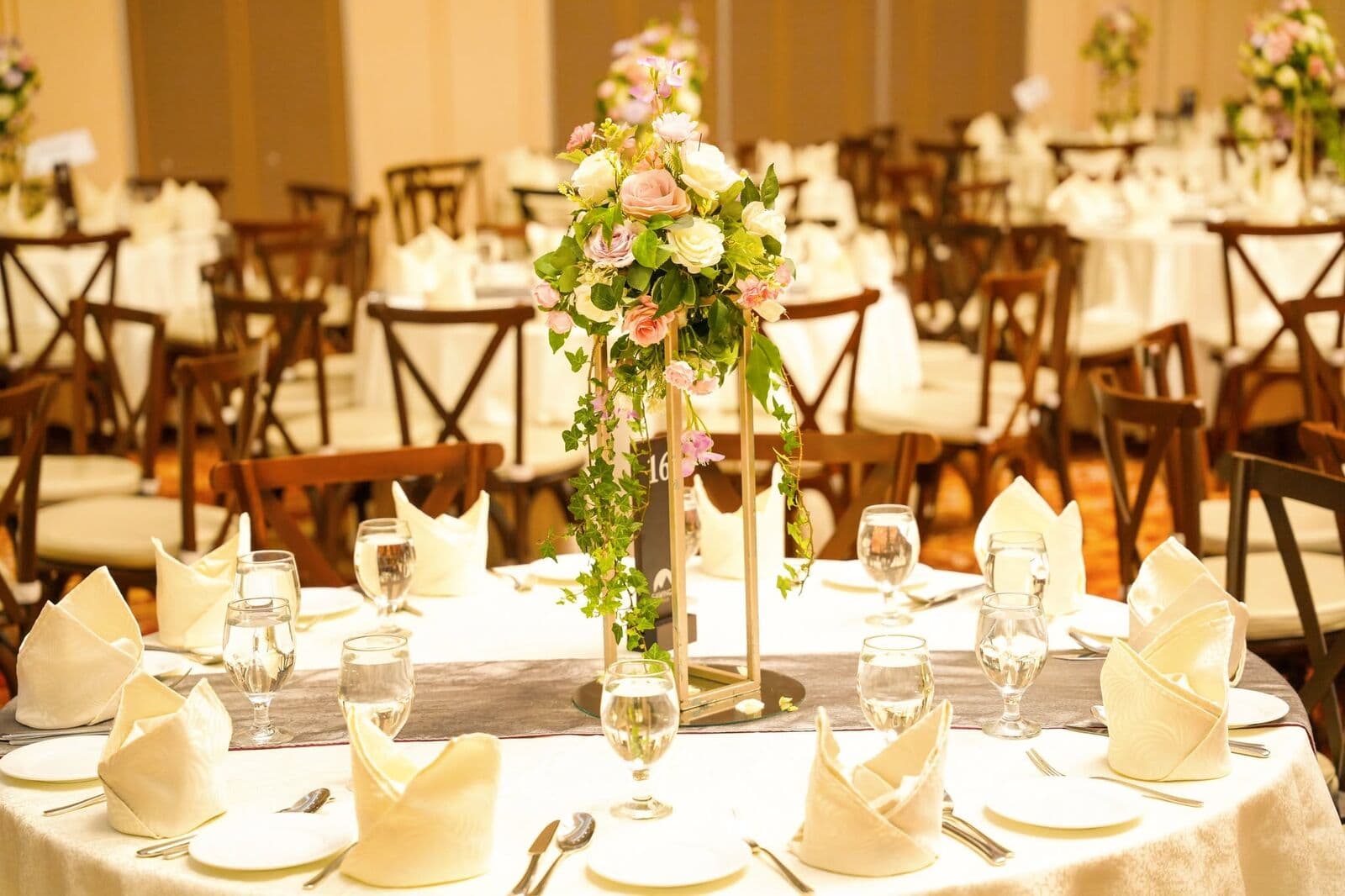 A tall centrepiece of pink roses on a table set with white napkins