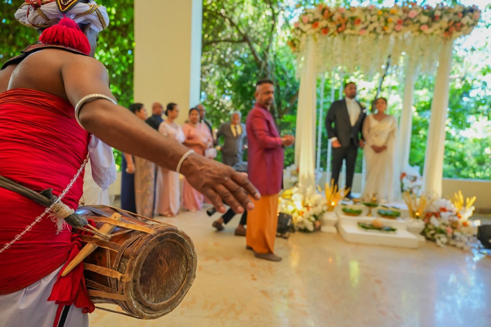 A drummer playing beside the poruwa as the couple and families gather