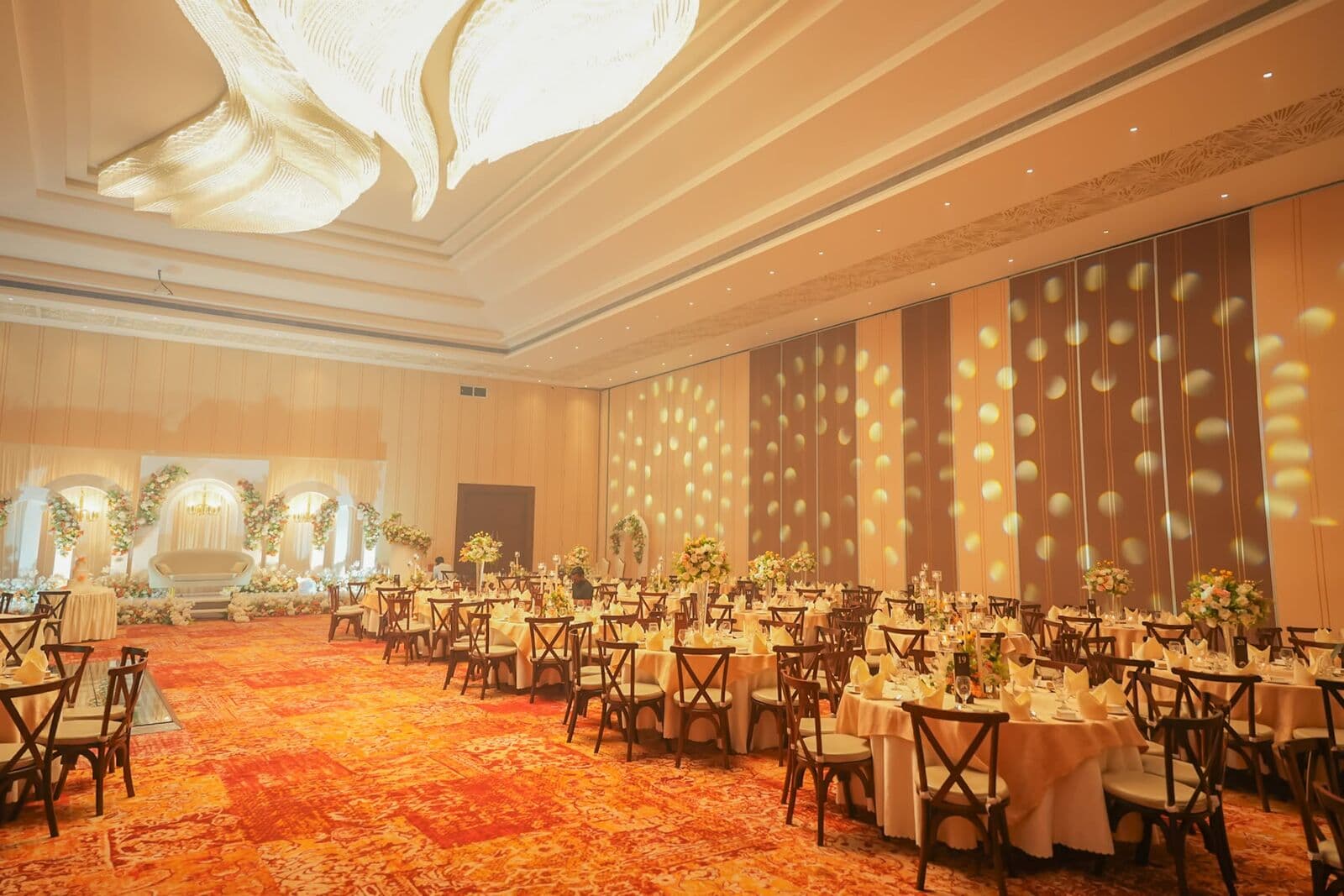 A large hall laid for a wedding, with warm lights on the walls and a glowing ceiling