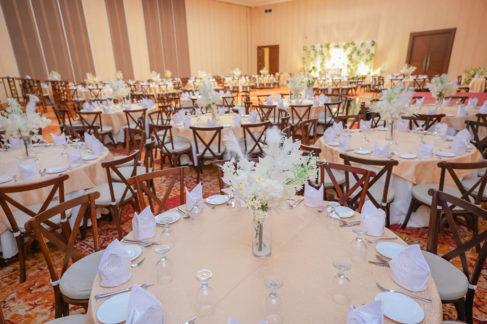 Round tables set with white flowers and wooden chairs in a hall