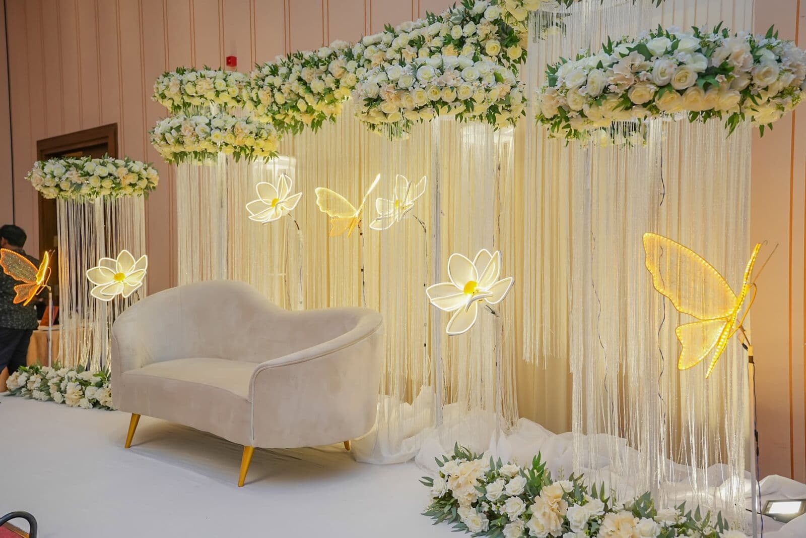 A white stage with a cream sofa, hanging flowers and glowing butterflies