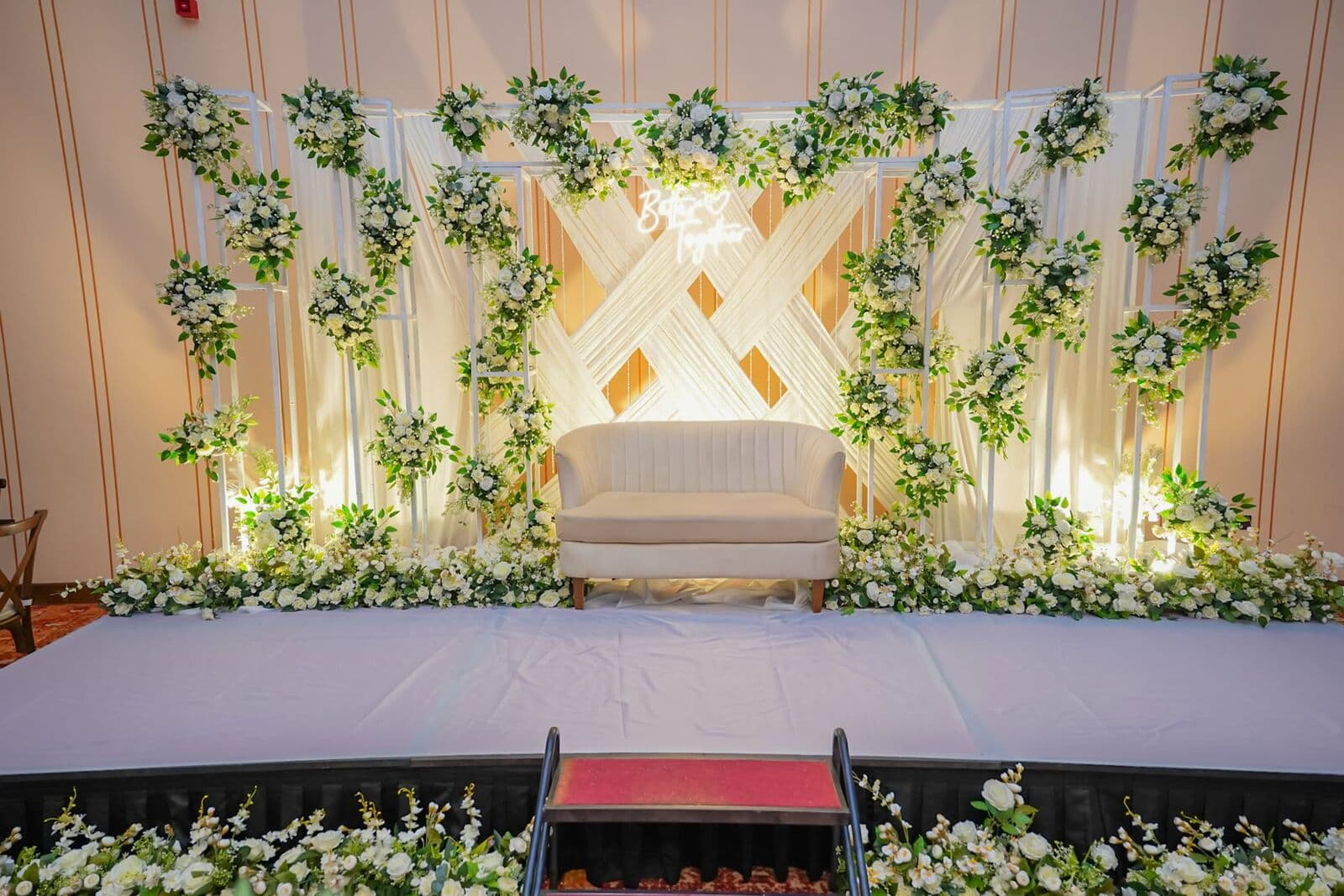 A stage with a cream sofa against a wall of white flowers and greenery