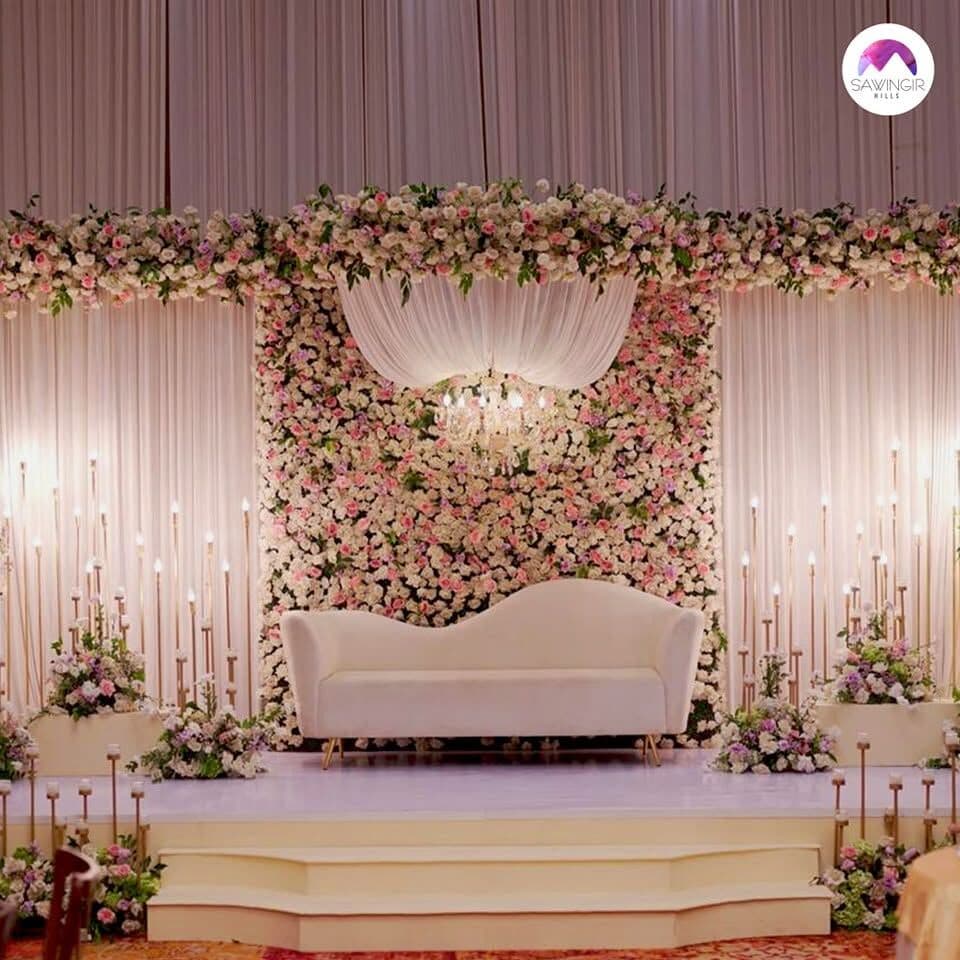 A stage with a white sofa in front of a wall of pink roses and candles