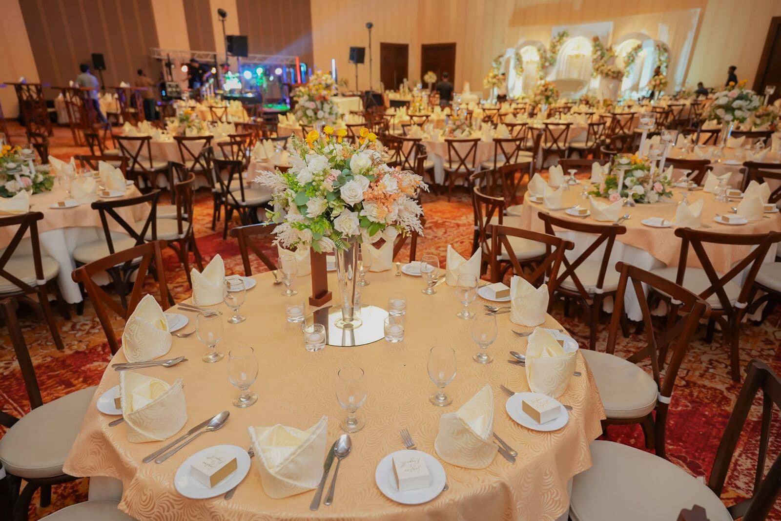 A round table with folded napkins and a tall vase of white and peach flowers