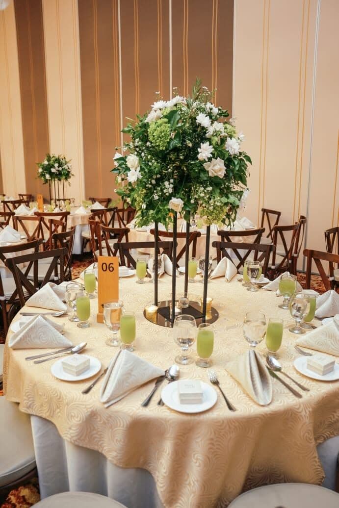 A round table with a tall centrepiece of white flowers and greenery