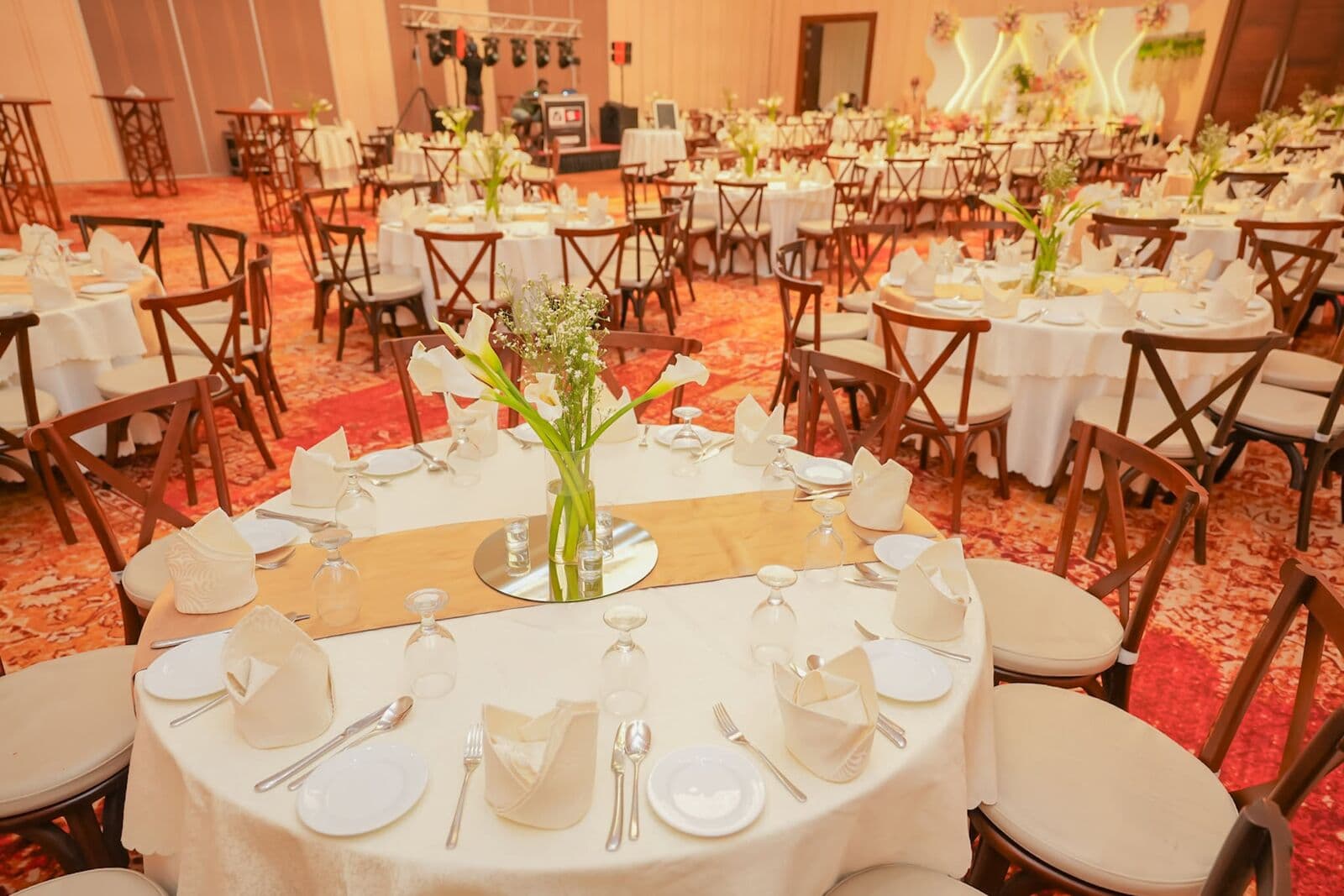 A round table set with white napkins, glasses and a tall flower centrepiece
