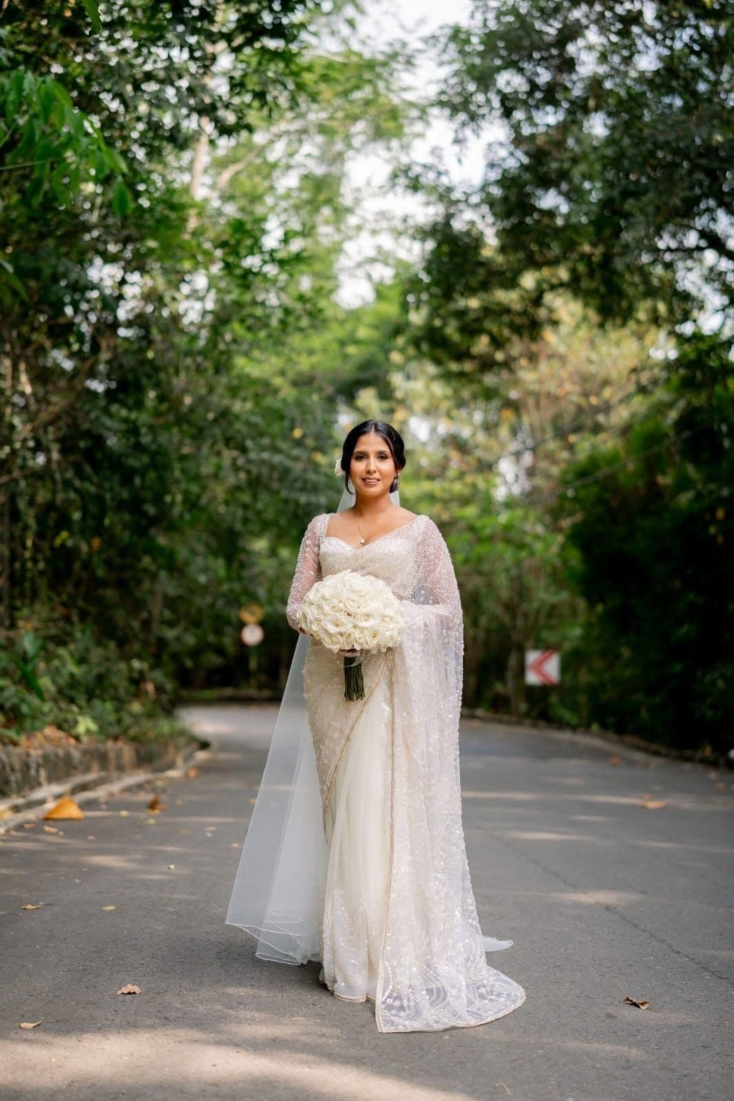 A bride in a white saree and veil on the drive under the trees