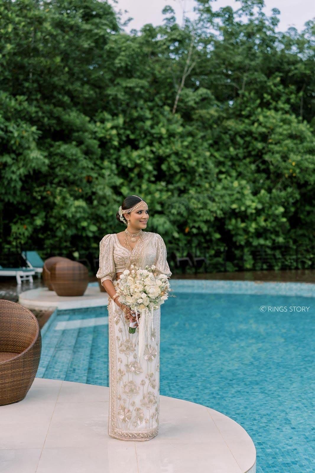 A bride holding white roses at the edge of the pool, with the forest behind