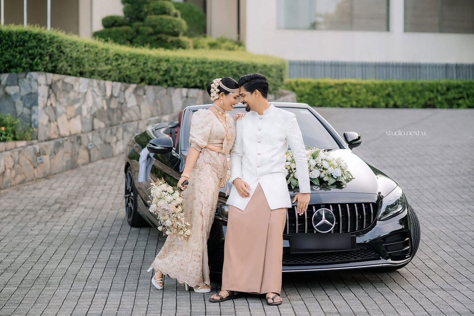A couple leaning on a flower-decked black car on the drive