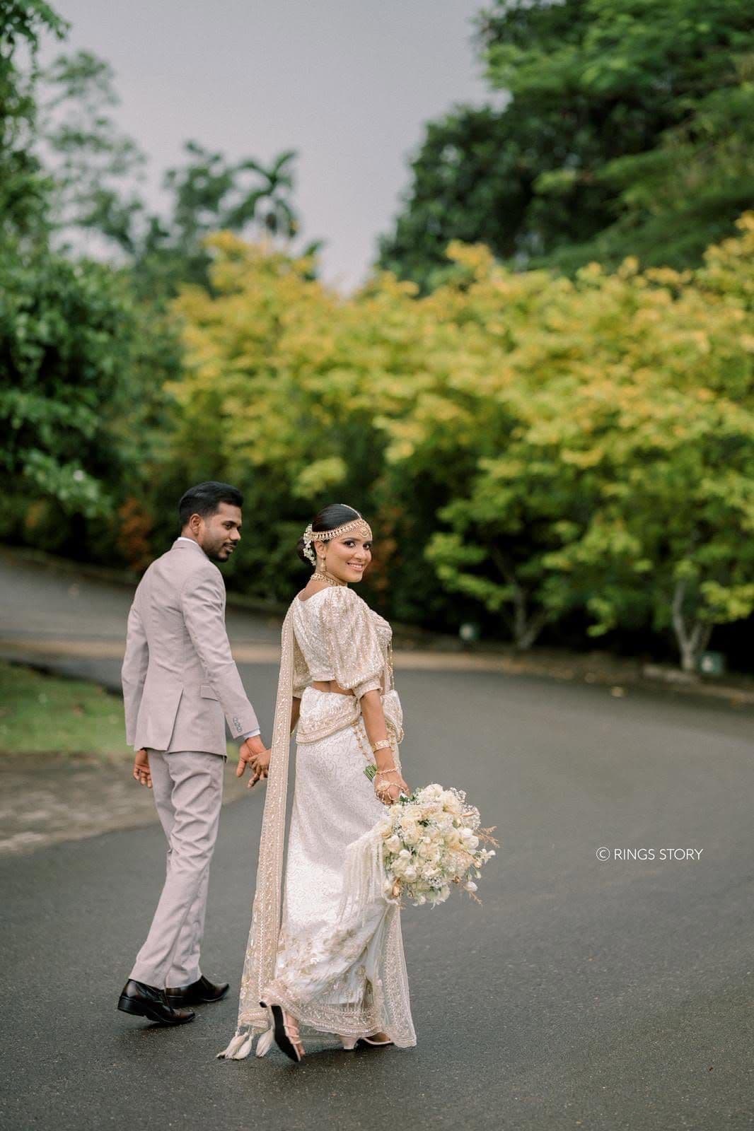 A bride and groom walking hand in hand up the tree-lined drive