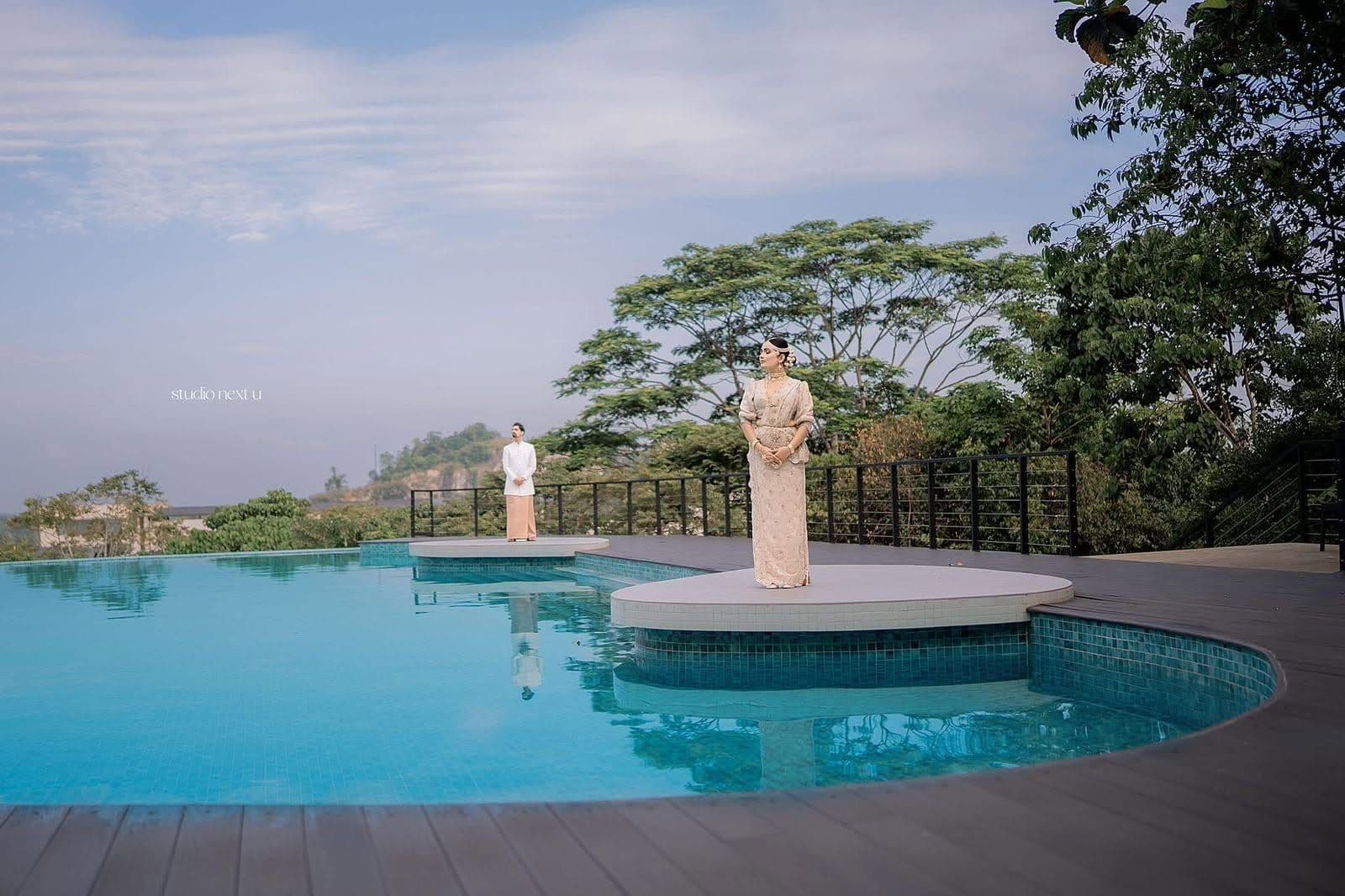 A bride and groom standing on the infinity pool's platforms, with trees and the hills behind