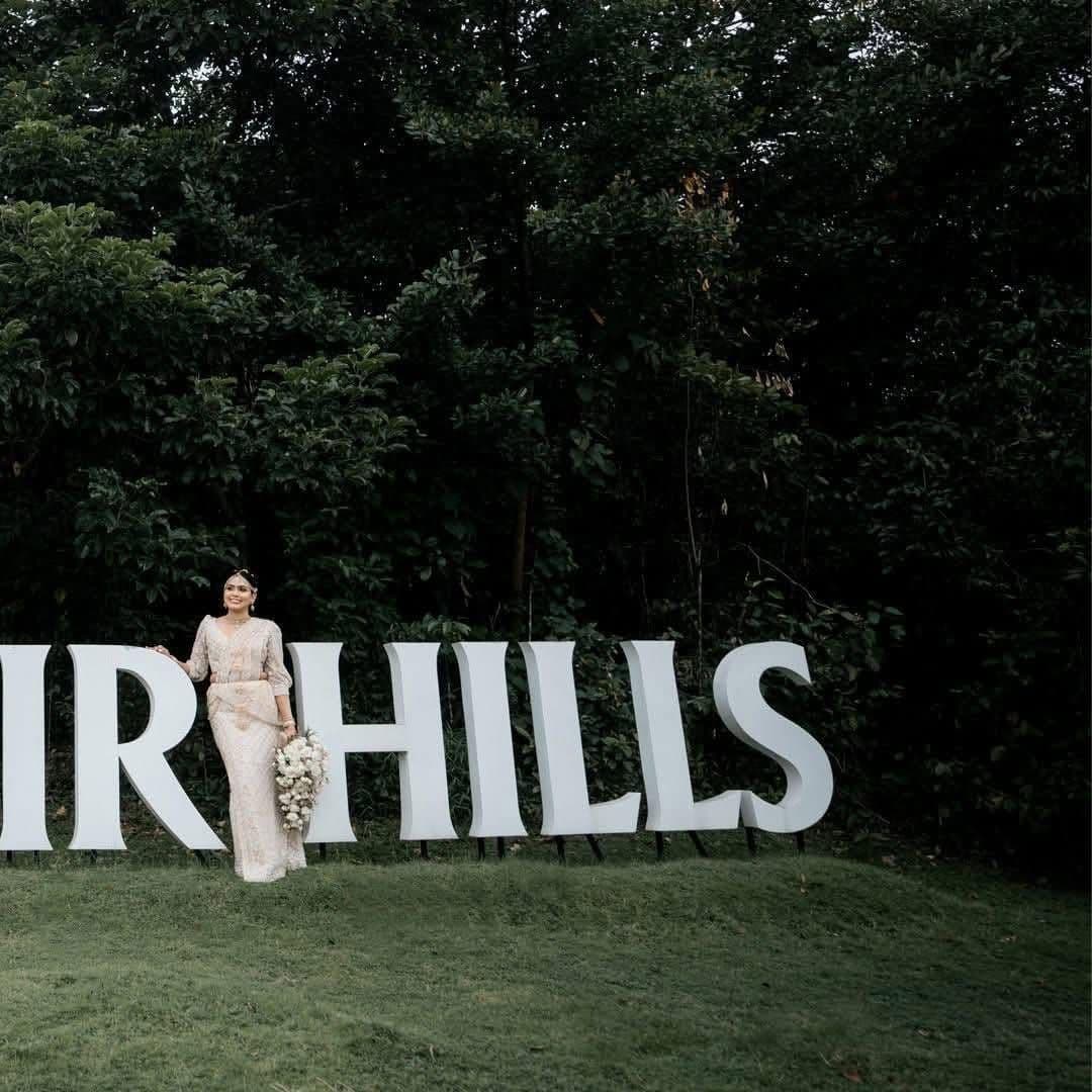 A bride leaning on the big white HILLS letters, with the forest behind
