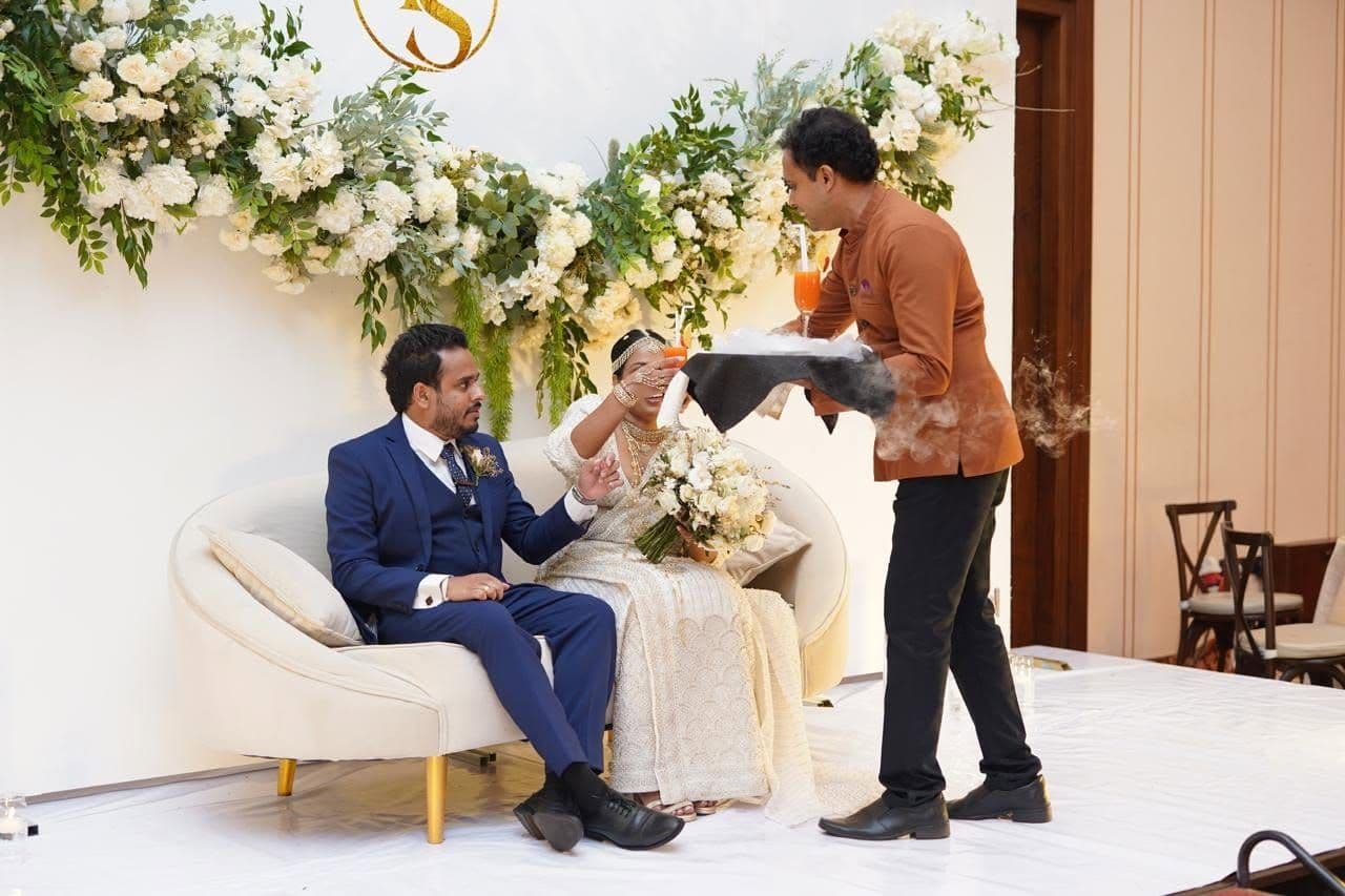 A waiter serving the couple smoking welcome drinks on their stage