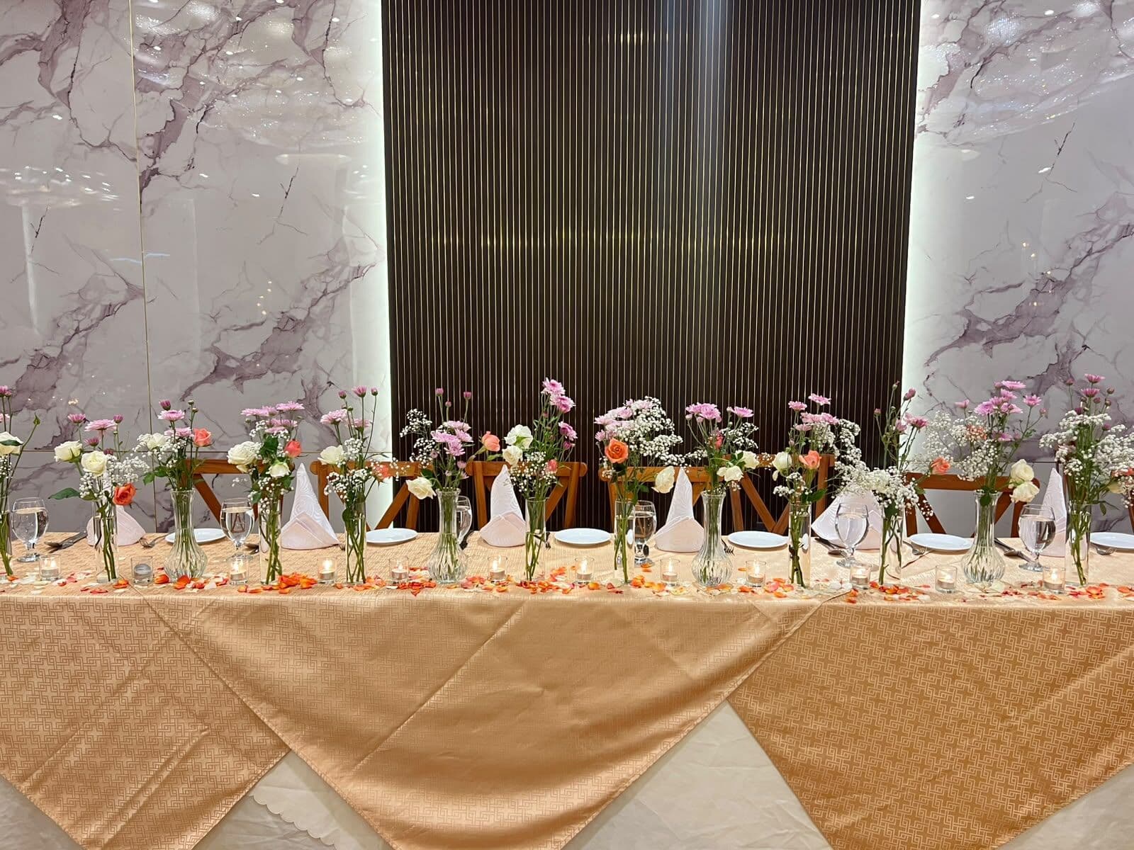 A long table of small vases of pink and white flowers in Wisteria