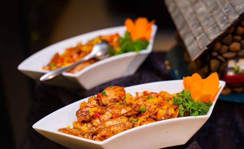 Two white bowls of spiced chicken dishes garnished with carrot